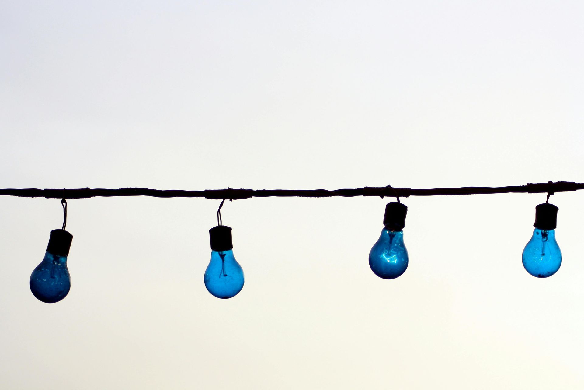 String of four blue lightbulbs against a white sky.
