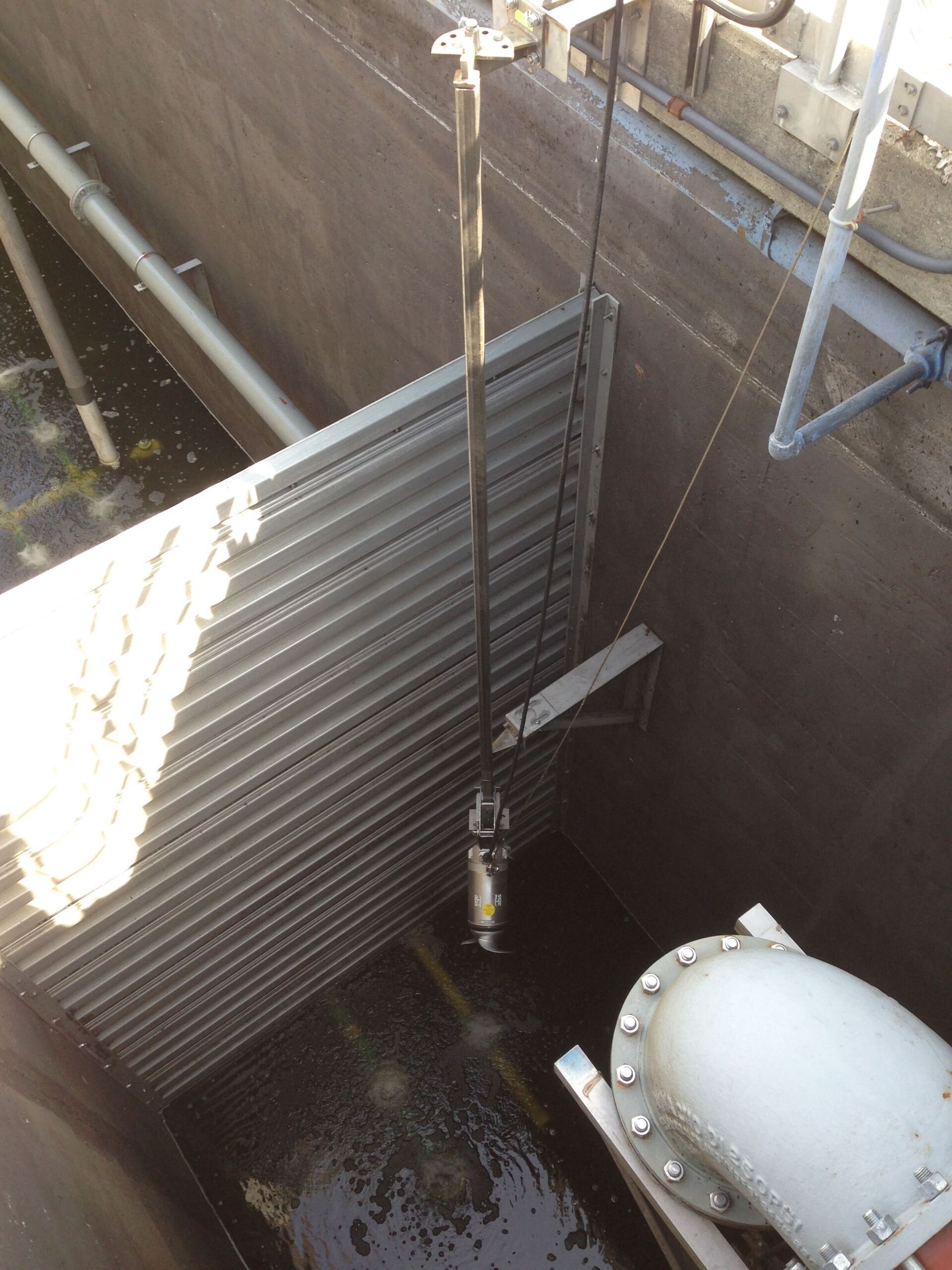 A white pipe is connected to a metal wall