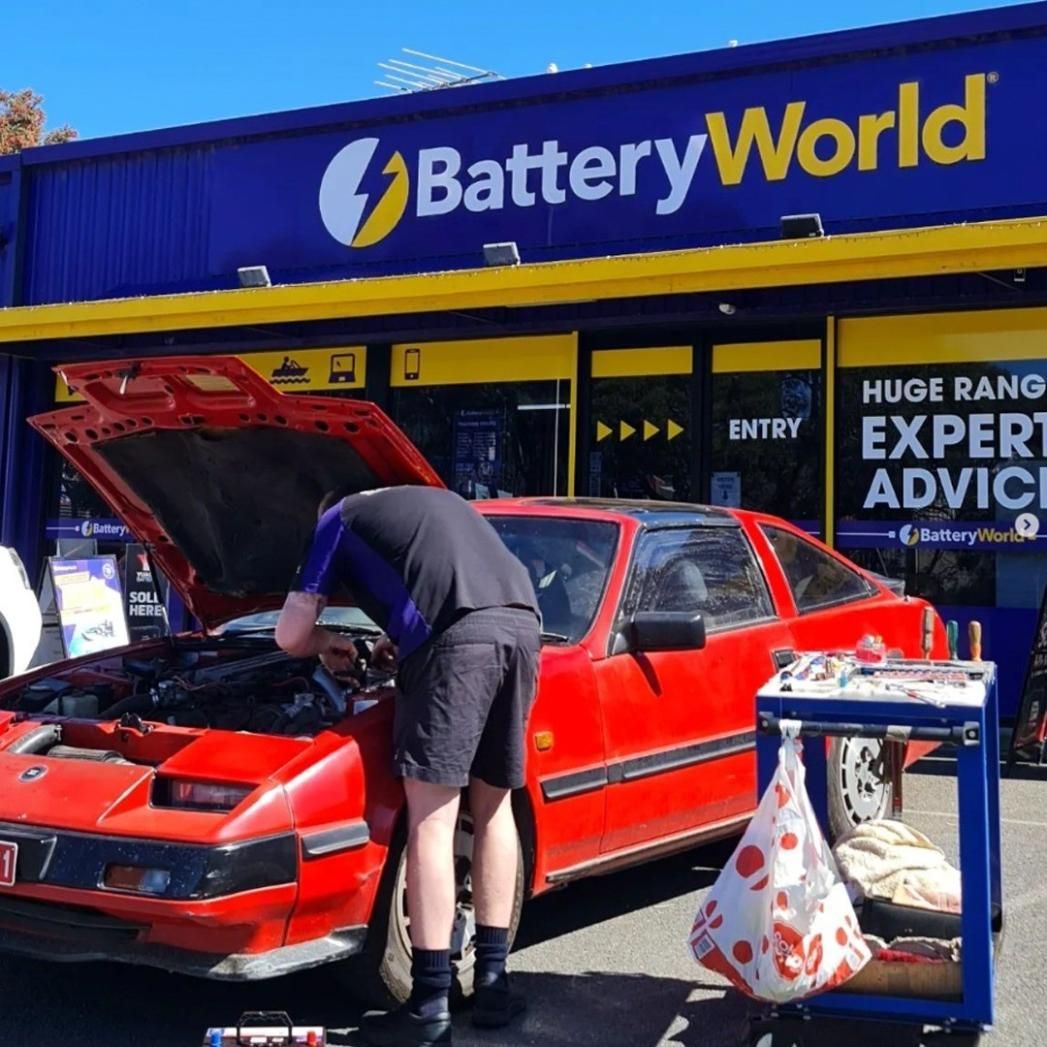 A Man is Working on a Red Car in Front of a Battery World Store — Battery World Townsville In Garbutt, QLD