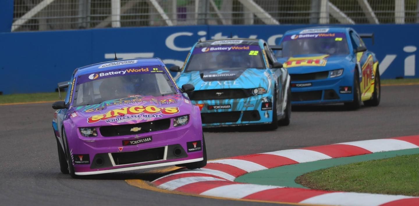 Three Racing Cars Are Driving Down a Race Track — Battery World Townsville In Garbutt, QLD