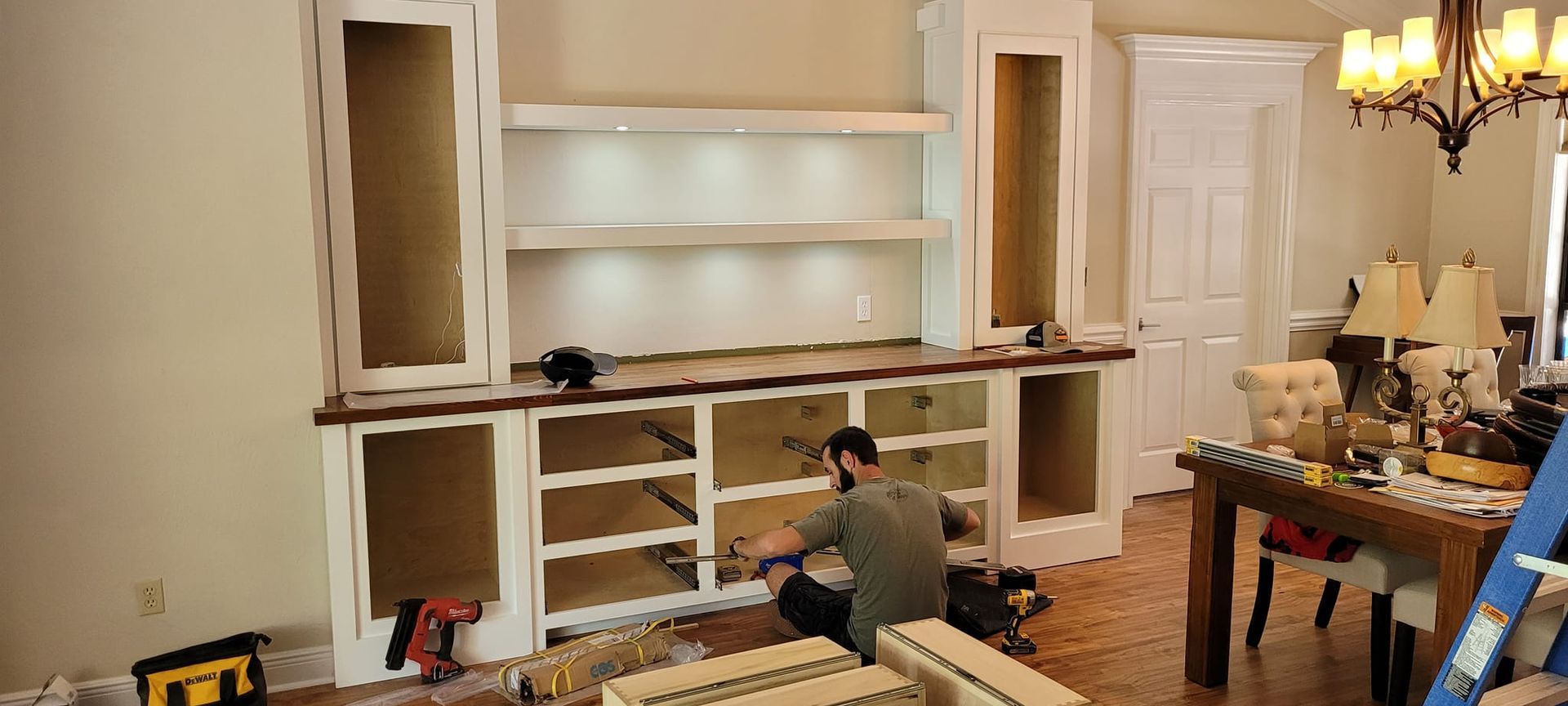 A man is sitting on the floor in a living room working on a cabinet.