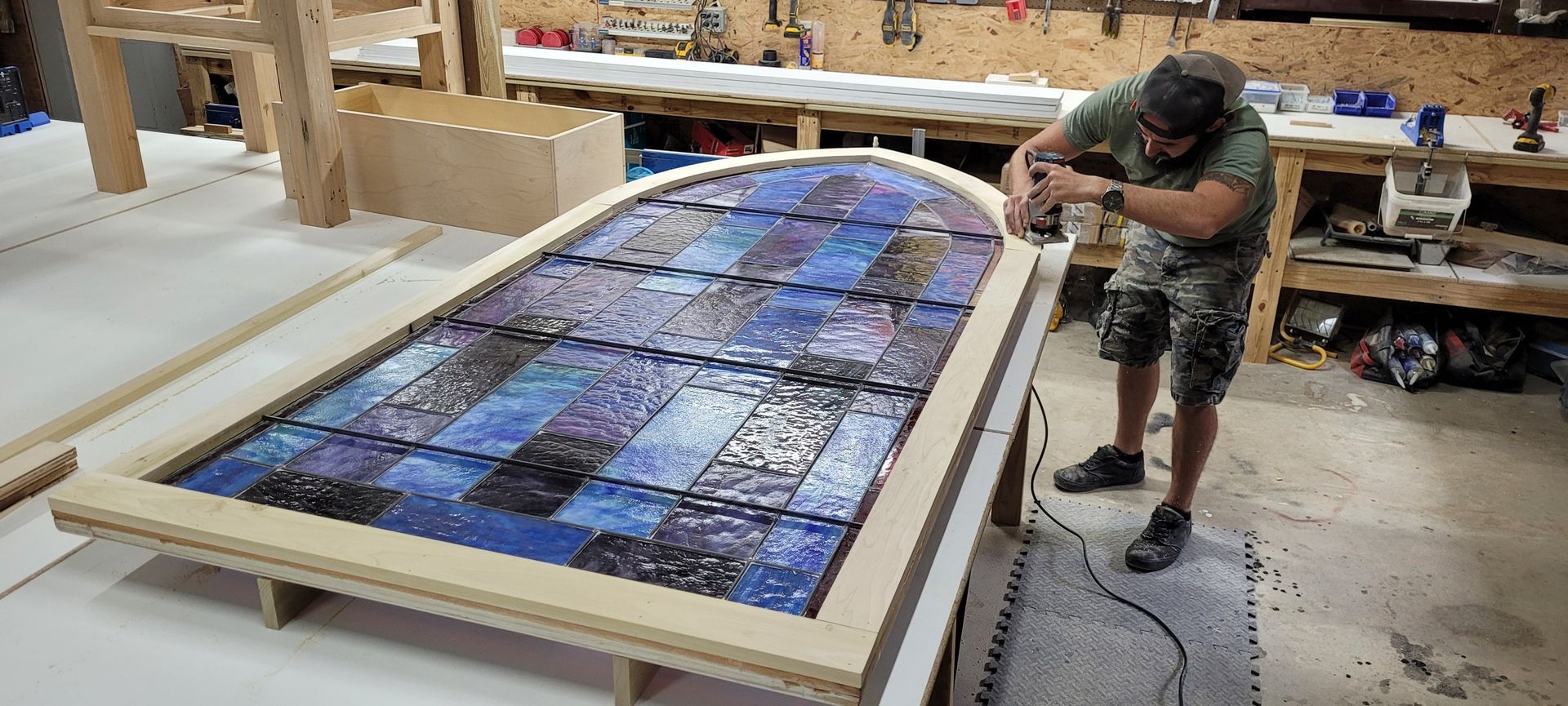 A man is working on a stained glass window in a workshop.