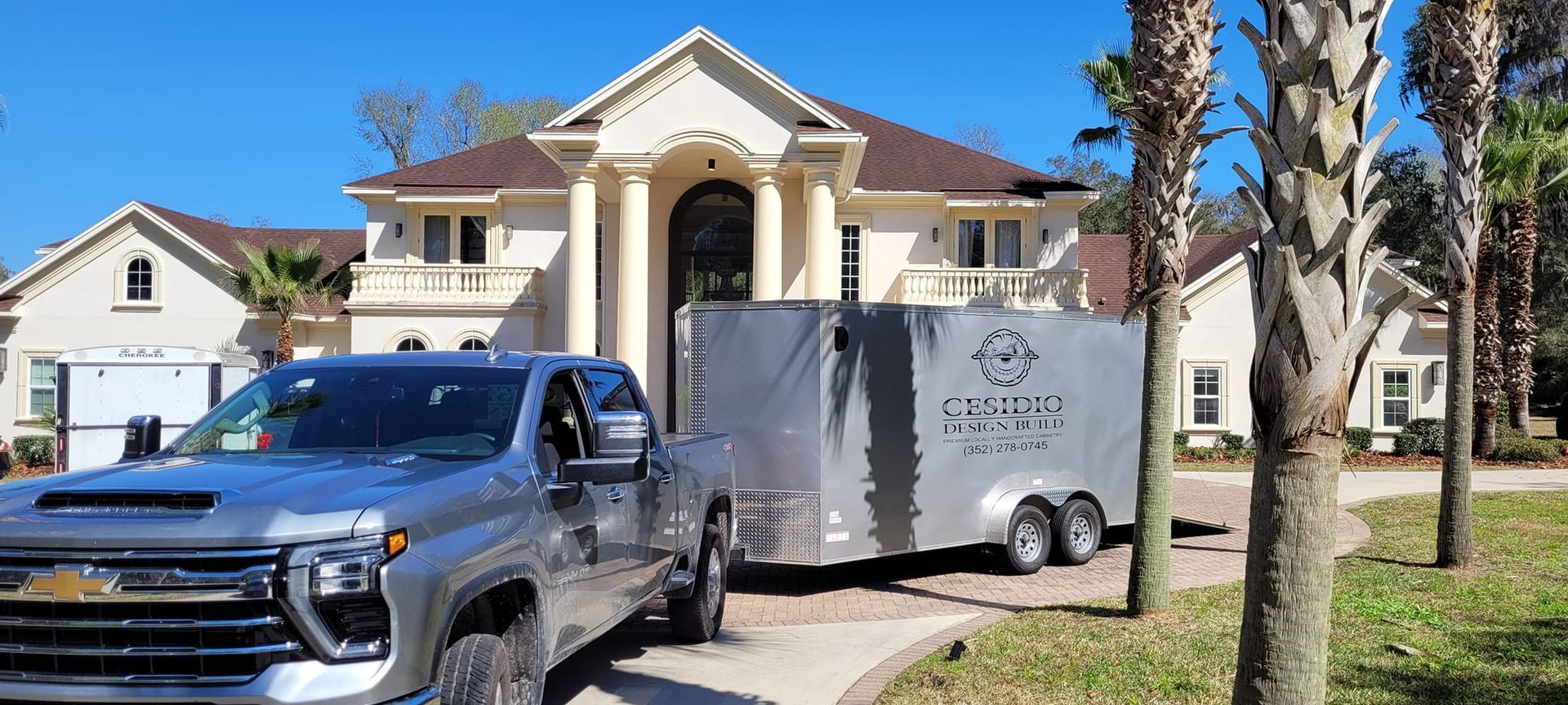 A truck is pulling a trailer in front of a large house.