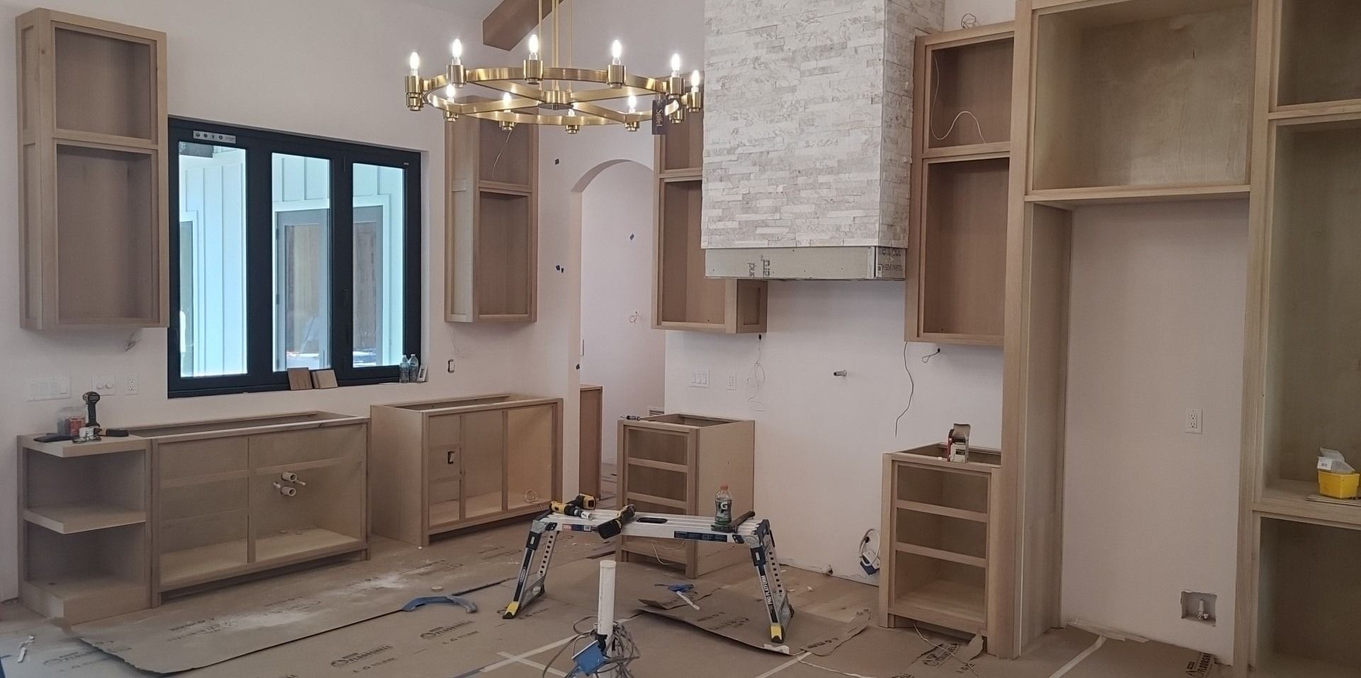 A kitchen under construction with wooden cabinets and a chandelier.