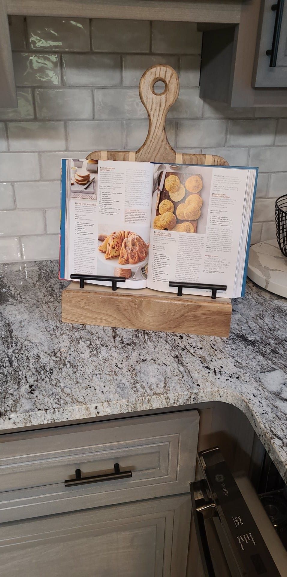 A cookbook is sitting on a wooden stand on a kitchen counter.