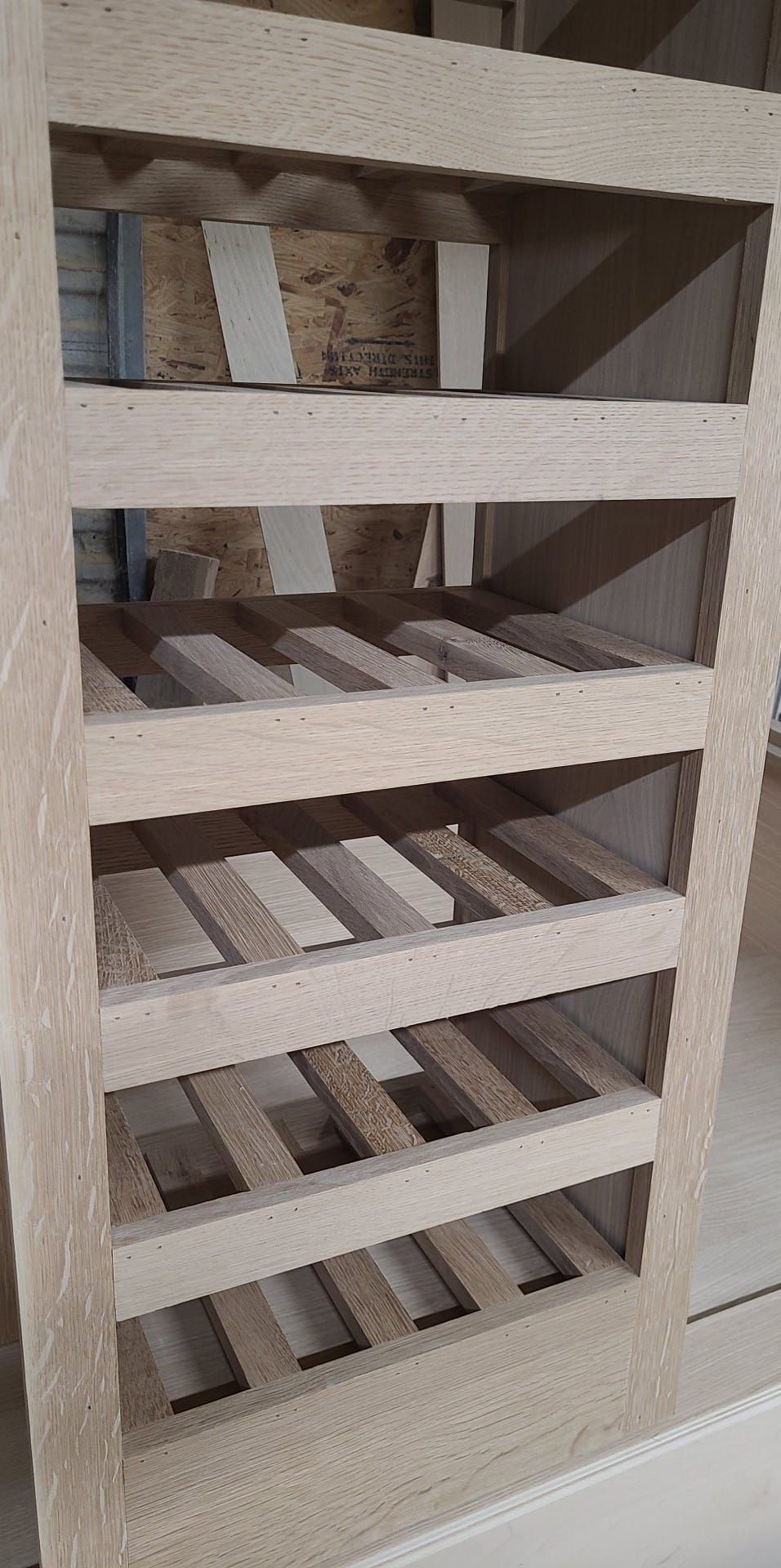 A wooden shelf with a lot of shelves and a staircase in the background.