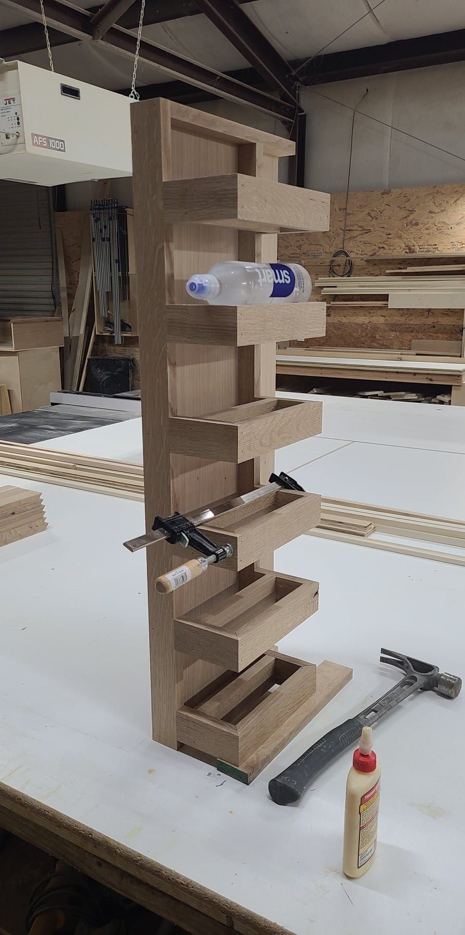 A wooden shelf with a bottle of glue and a hammer on a table.