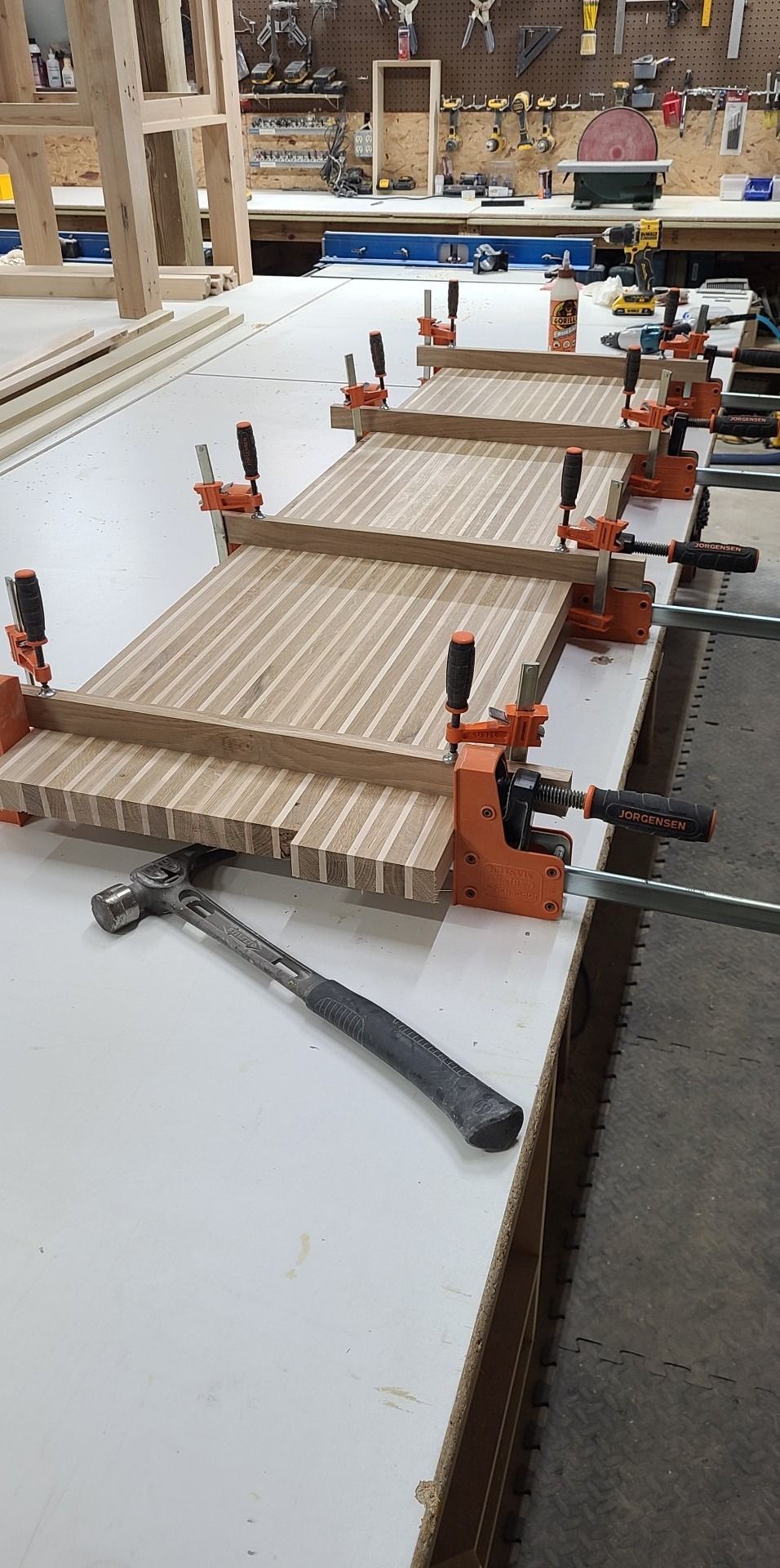 A wooden table is being glued together with clamps and a hammer.