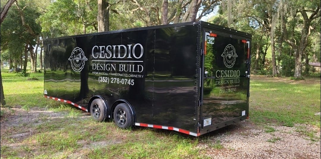 A black trailer is parked in a grassy field.