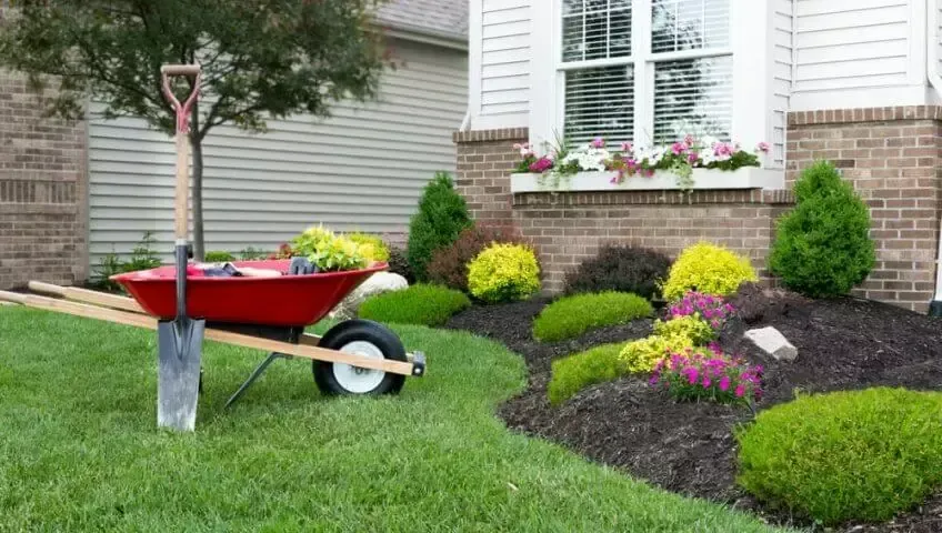 A wheelbarrow with a shovel attached to it is parked in front of a house.