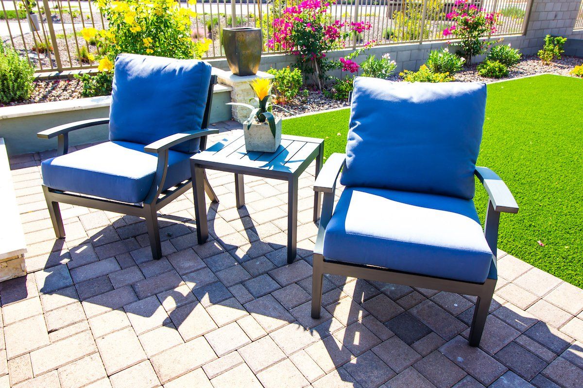 Two blue chairs and a table on a brick patio.