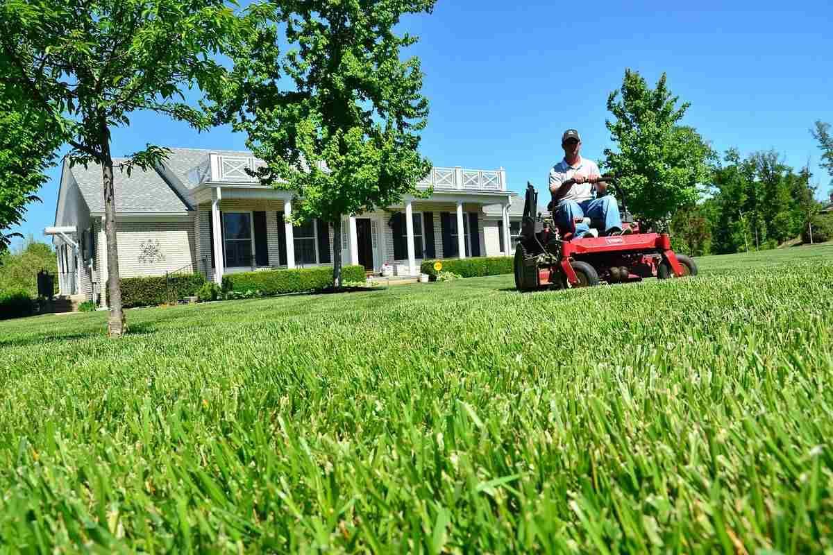 A man is riding a lawn mower in front of a house.