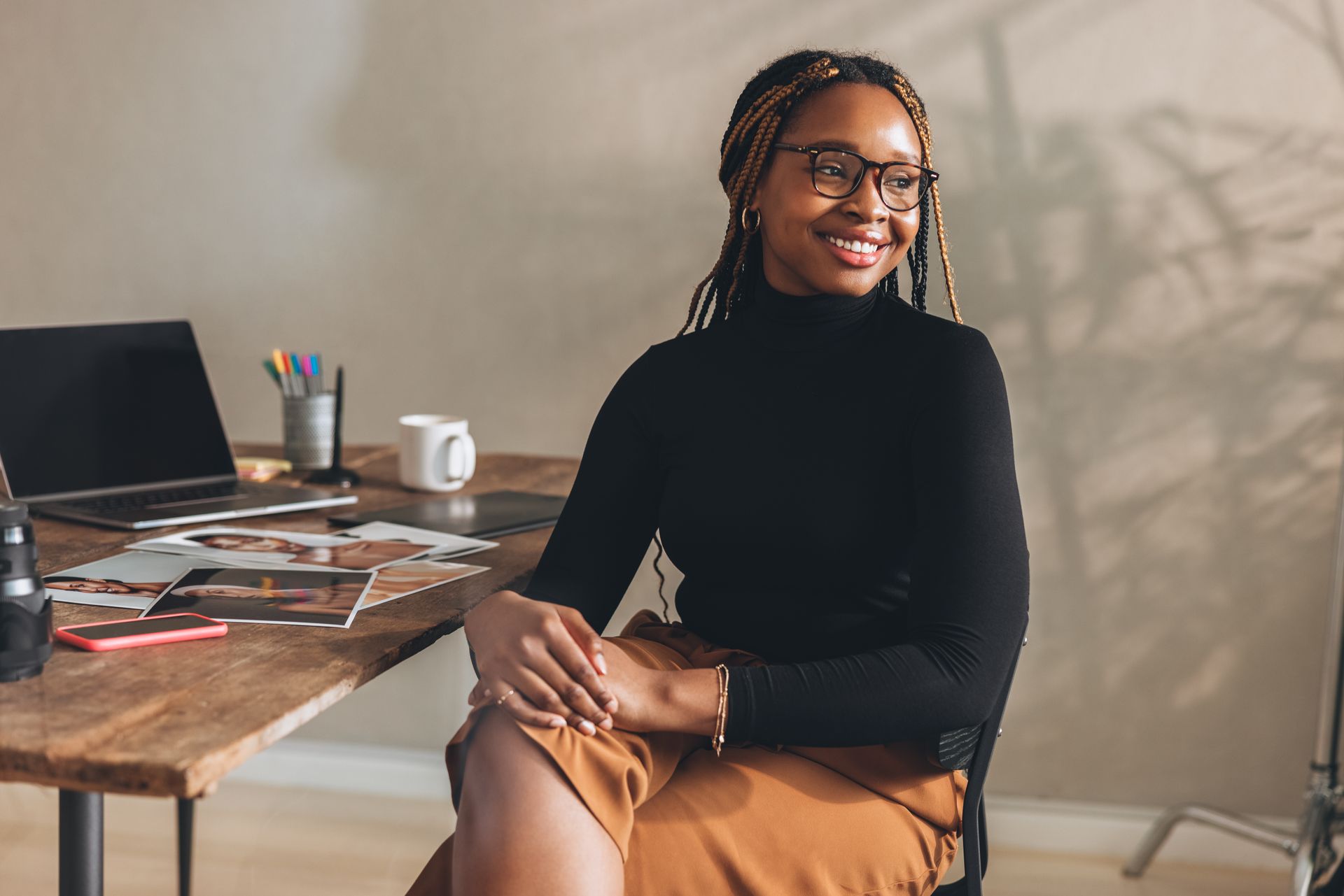 A woman is sitting at a desk with her legs crossed and smiling.