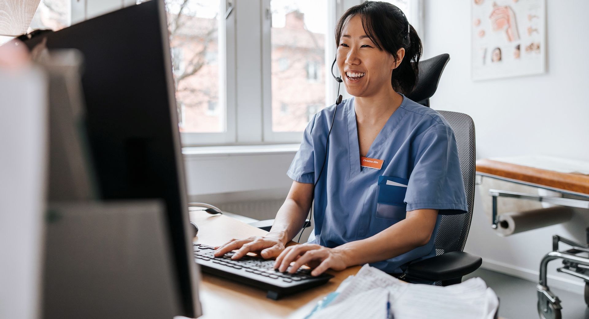 A nurse is sitting at a desk in front of a computer.