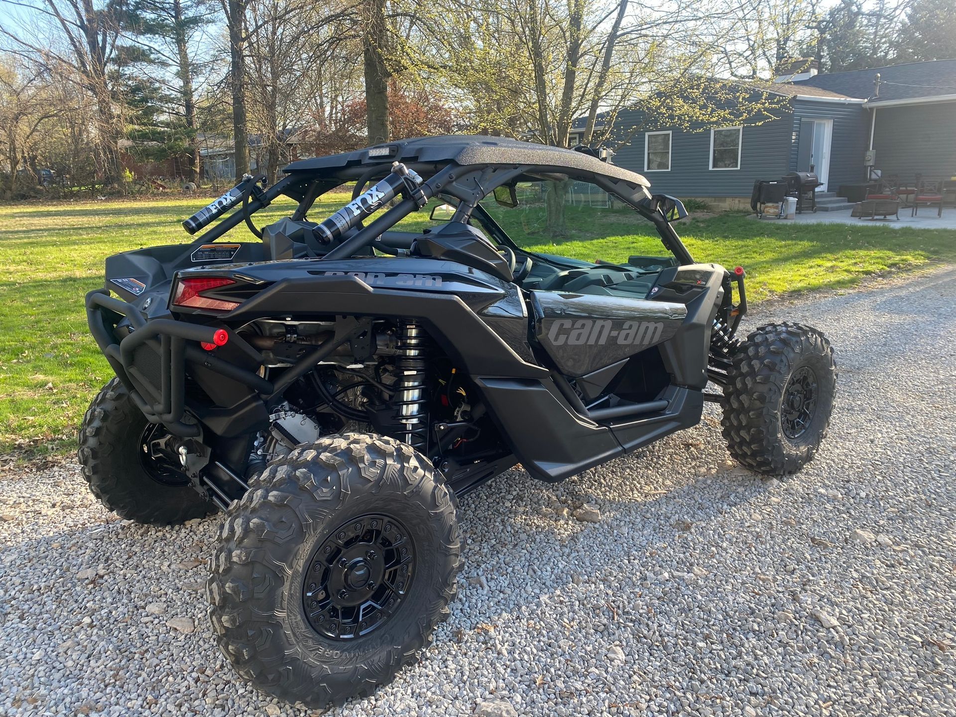A can am maverick x3r is parked on a gravel road in front of a house.