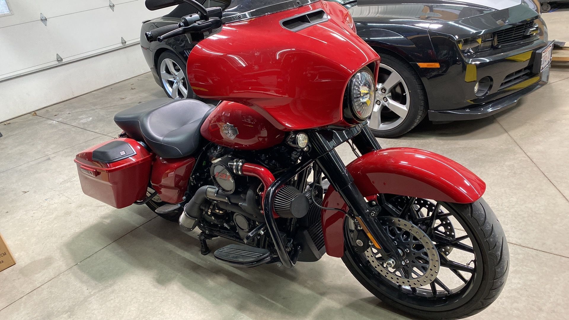 A red motorcycle is parked next to a black car in a garage.