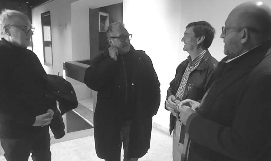 Four people in coats converse inside a building.