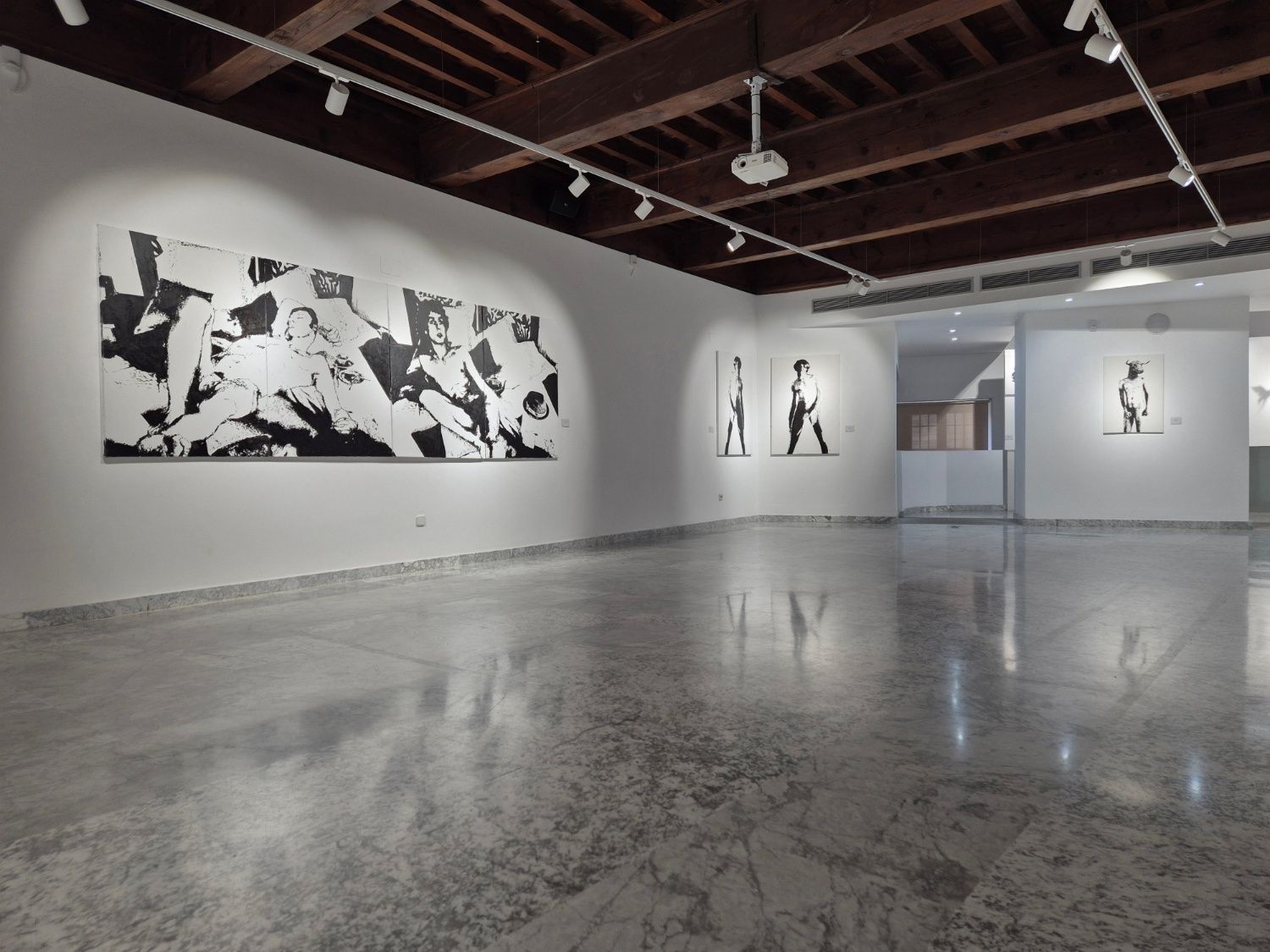Art gallery interior featuring black and white artwork on white walls. Polished concrete floor, exposed wooden ceiling beams.