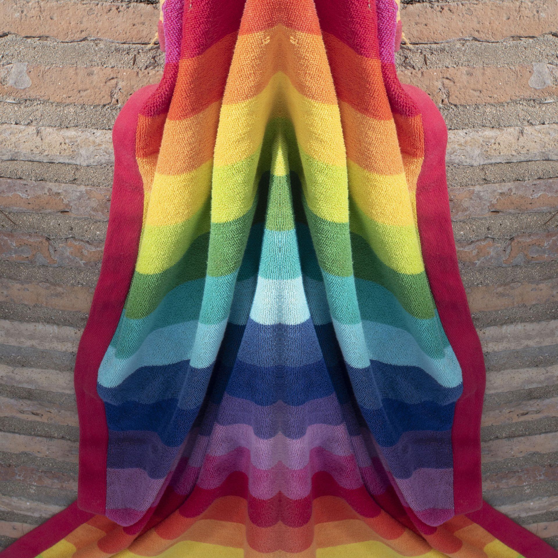 a rainbow-colored blanket is against a brick wall