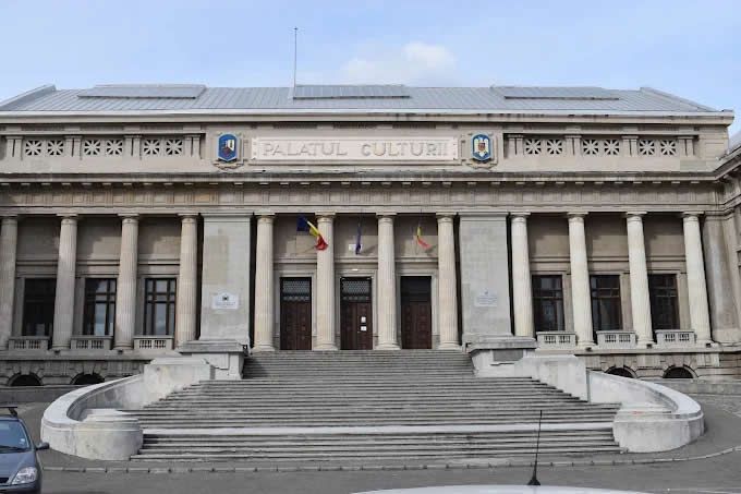 Exterior of the Palace of Justice building with stone columns, steps, and the Romanian flag.