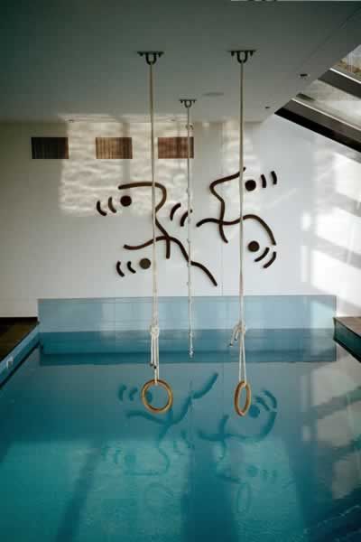 blue indoor swimming pool, with abstract wall art by Garbade reflecting in the water.