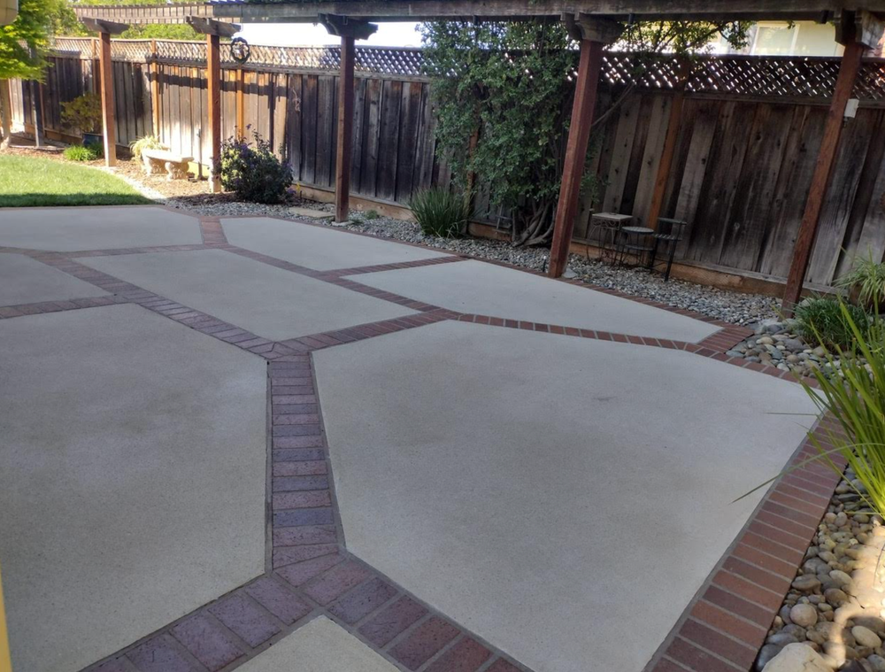 A brick and concrete driveway with a wooden fence in the background