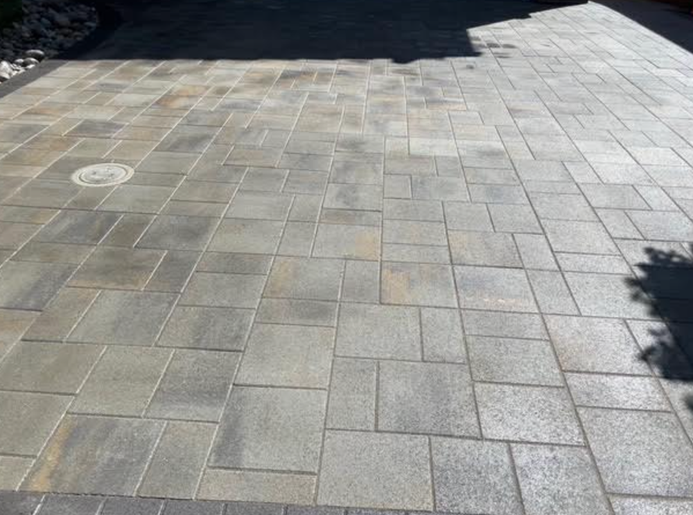 A brick driveway with a drain hole in the middle of it.