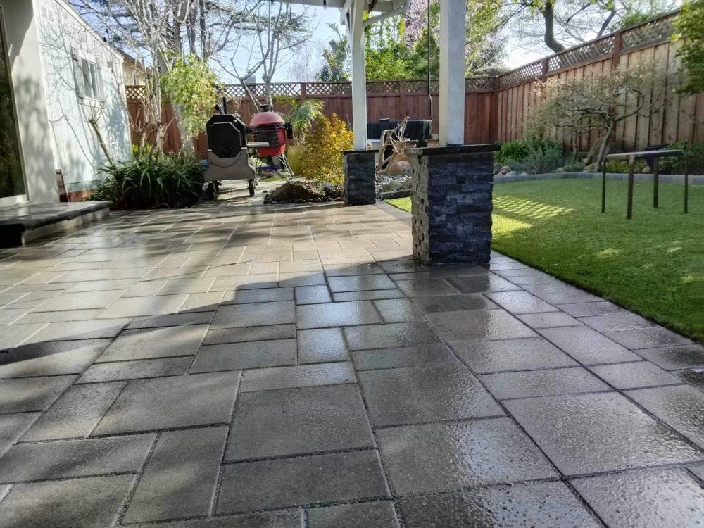 A patio with a fence in the background and a lawn in the foreground.