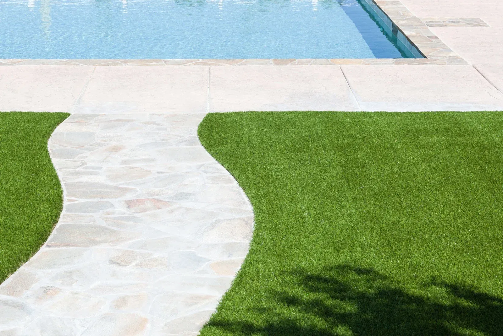 A walkway leading to a swimming pool surrounded by green grass.