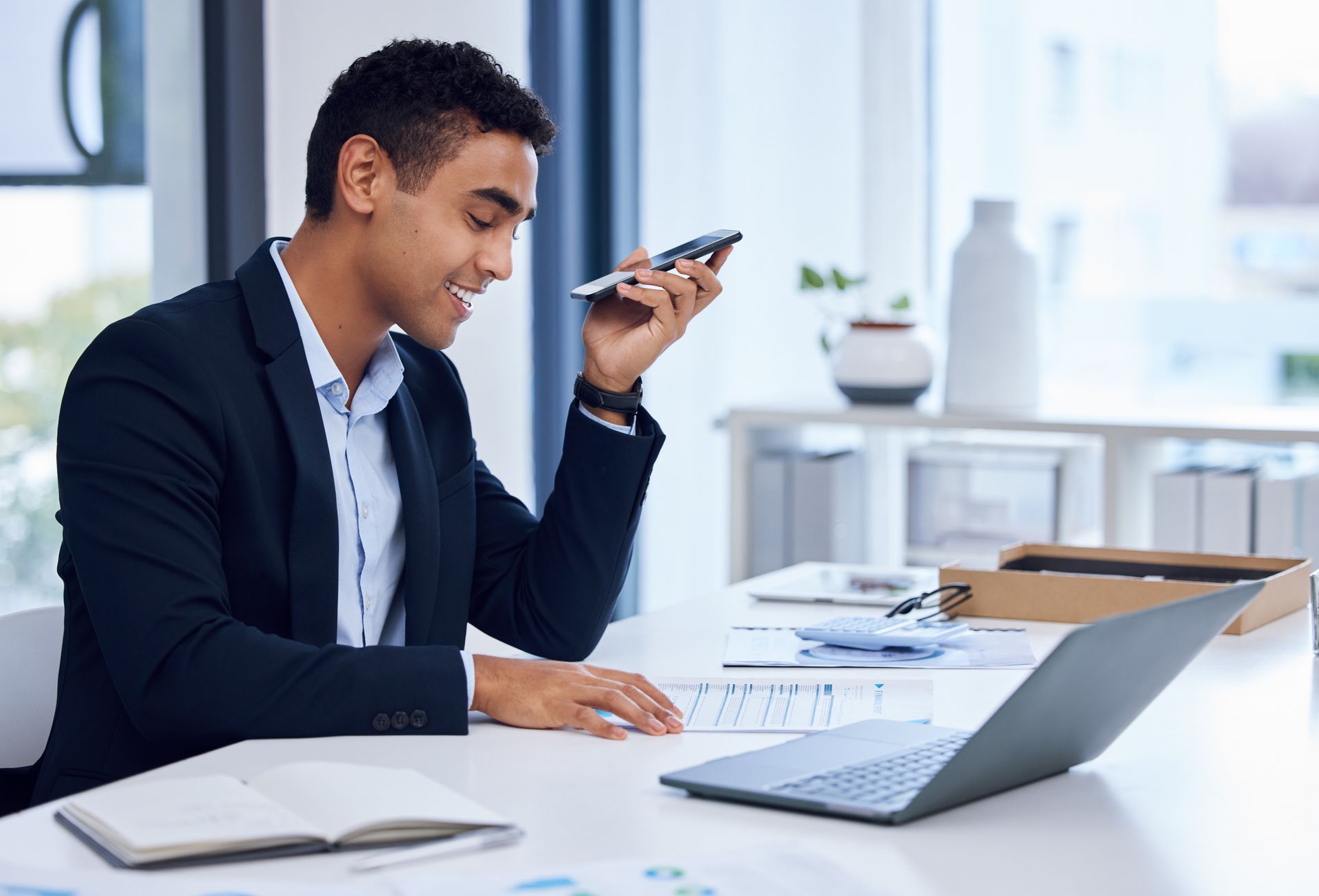 A man is sitting at a desk with a laptop and a cell phone.