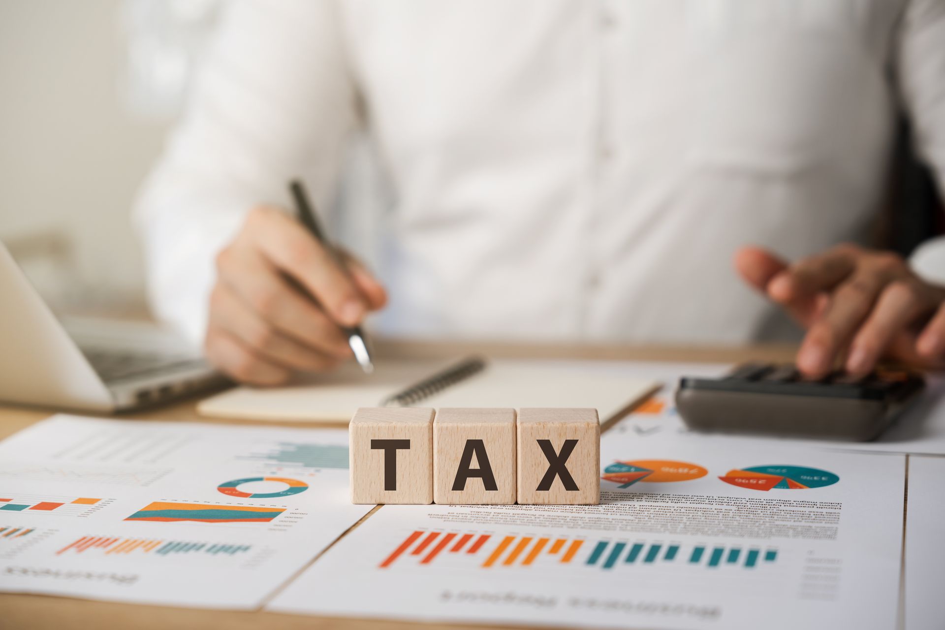 A person is sitting at a desk with a calculator and a wooden block with the word tax on it.