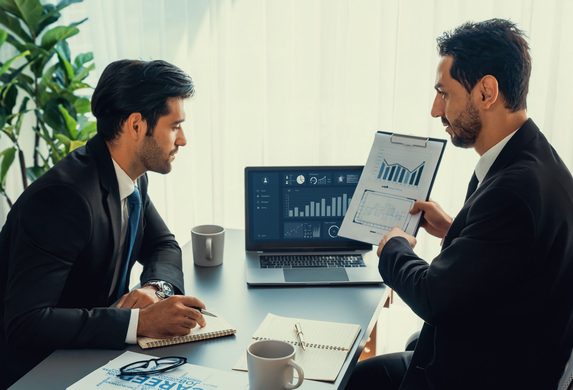 Two men are sitting at a table looking at a clipboard.