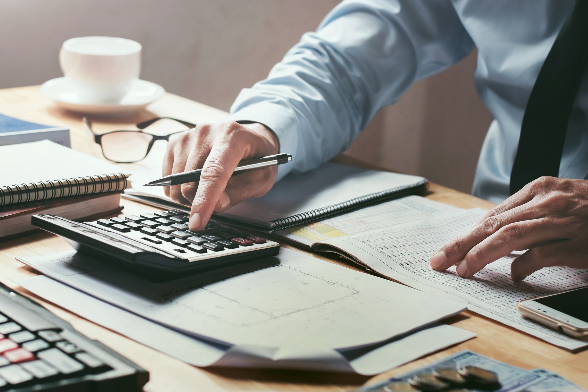 A man is sitting at a desk using a calculator and a pen.