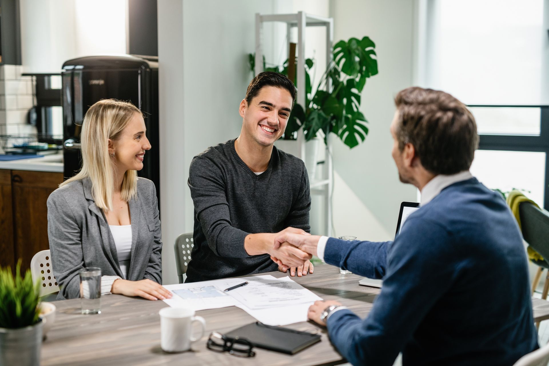 A man and a woman are shaking hands with a man while sitting at a table.