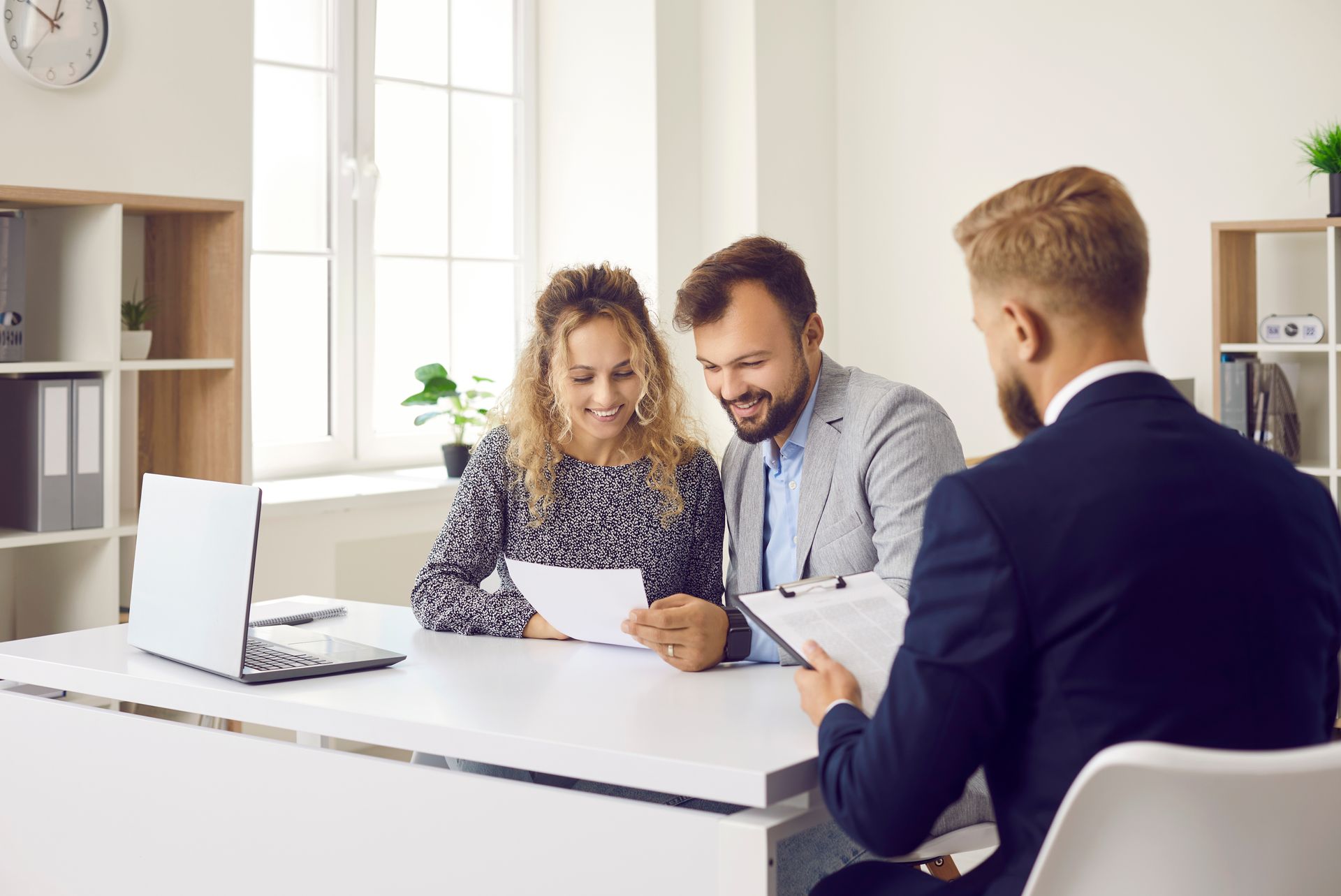 A man and a woman are sitting at a table talking to a man in a suit.