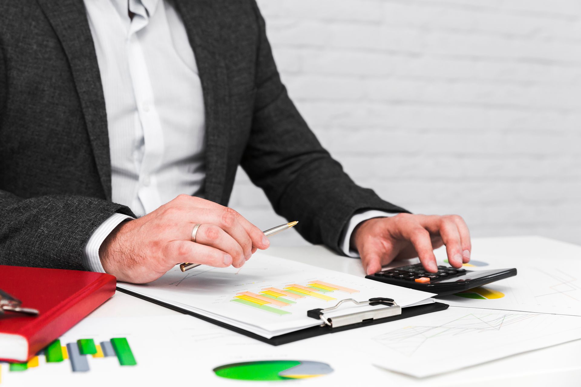Man in suit using calculator with charts and papers on a desk.