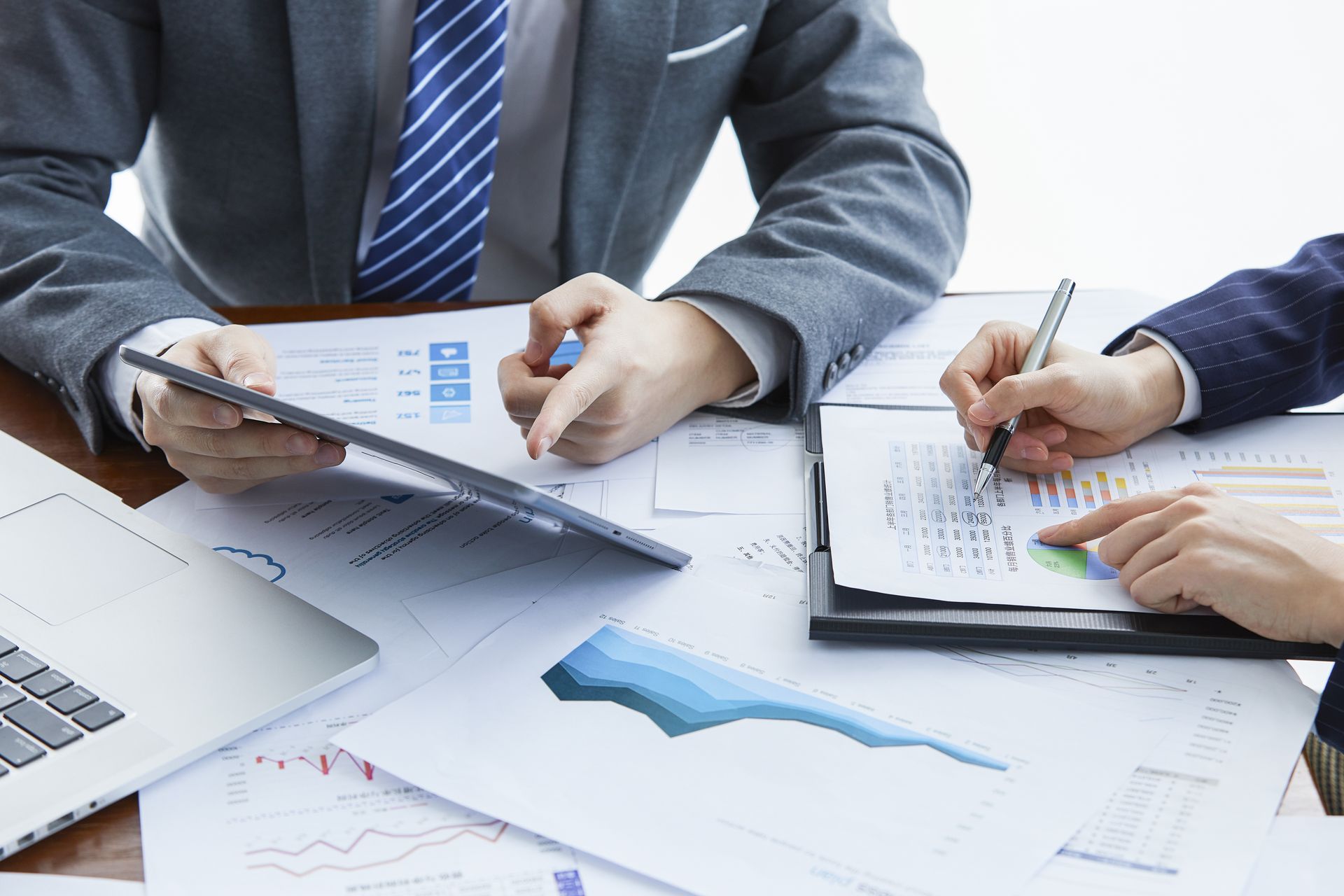 A man and a woman are sitting at a table with papers and a laptop.