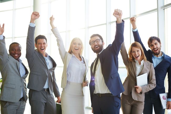 A group of business people are standing next to each other with their arms in the air.