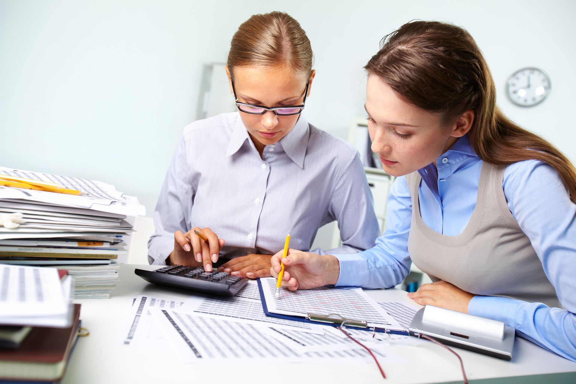 two women are sitting at a desk with papers and a calculator .