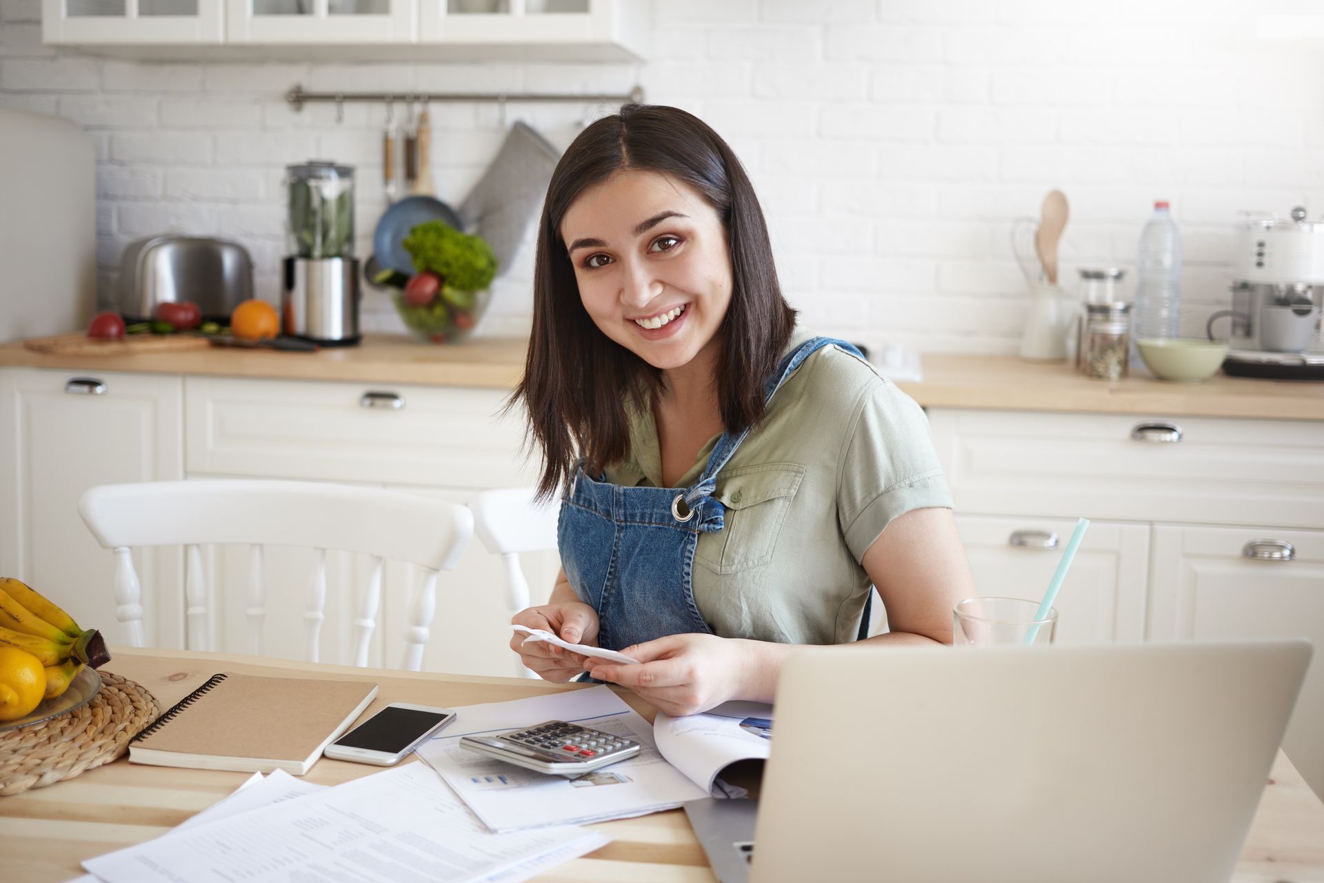 A woman is sitting at a table with a laptop and a cell phone.