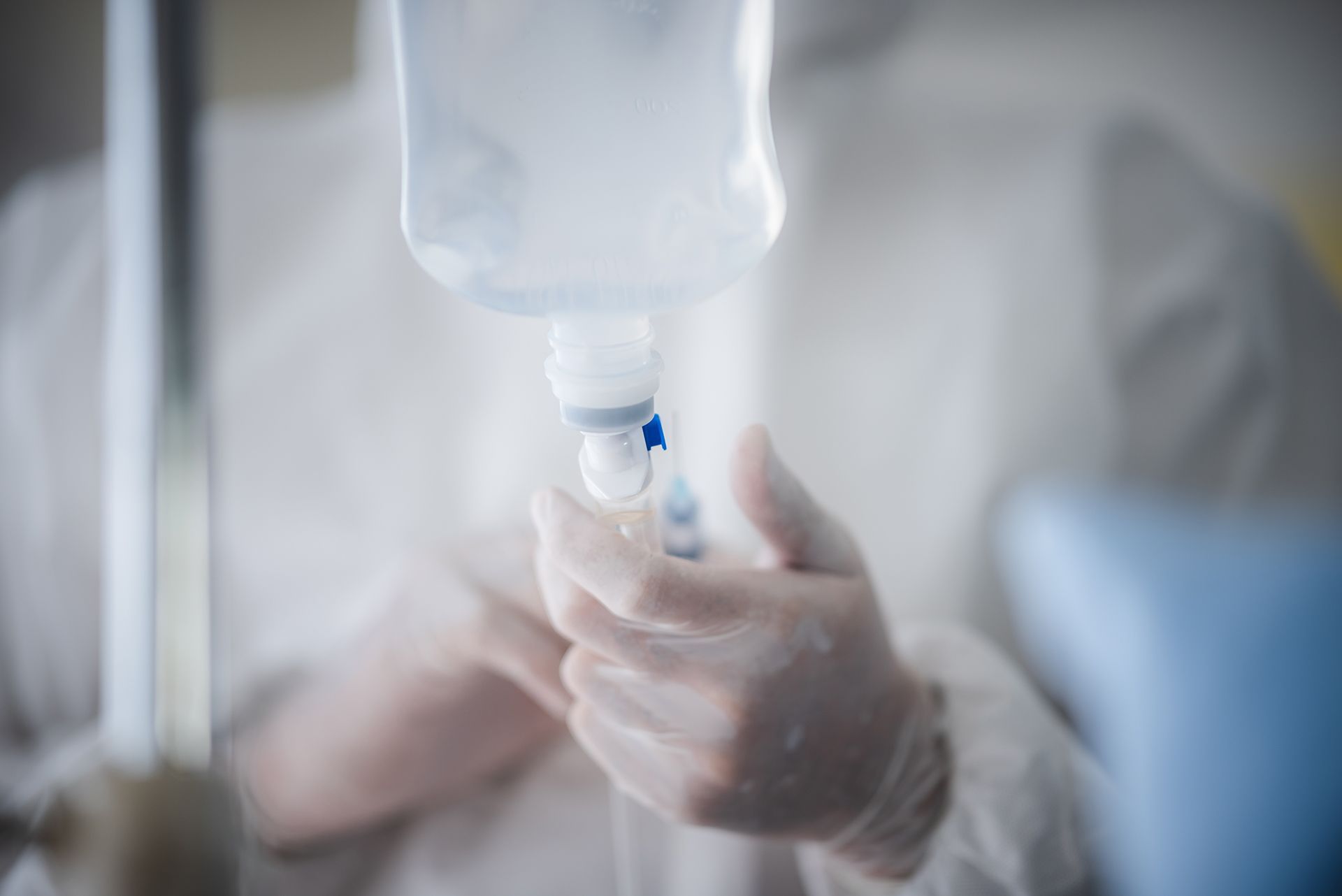 Gloved hands adjusting a saline IV bag in a clinical setting