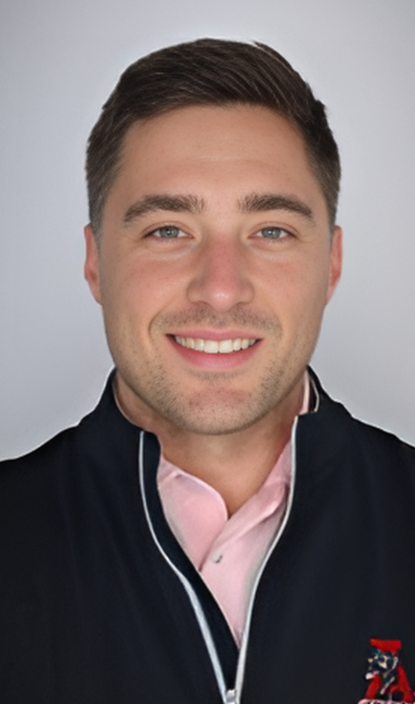 A man wearing a pink shirt and a black jacket is smiling for the camera.