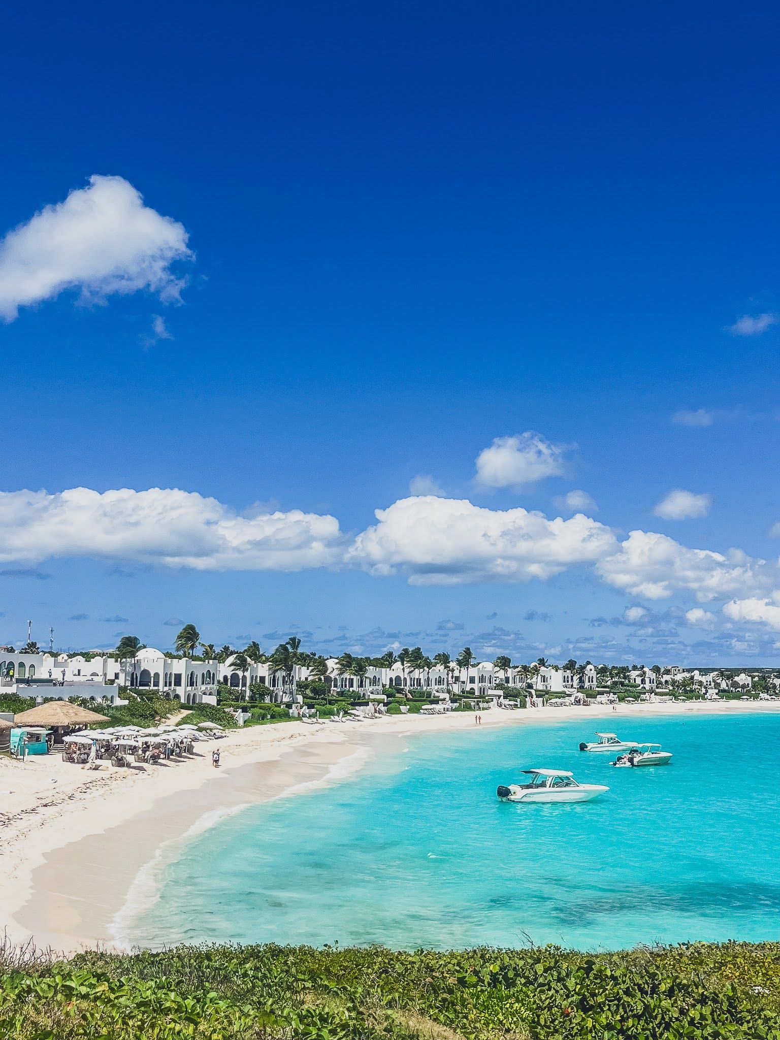 A beach with boats in the water and a blue sky