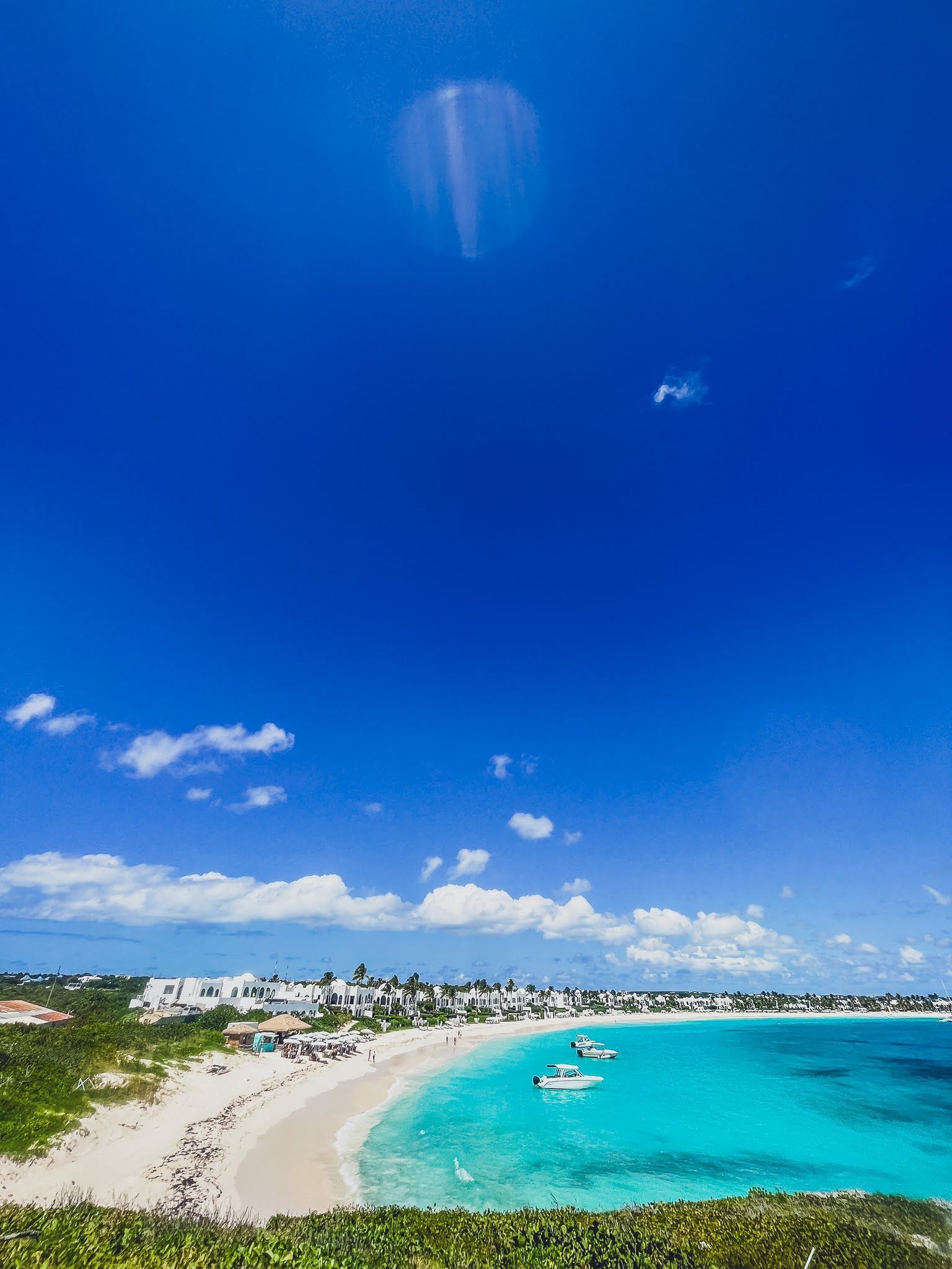 A beach with boats in the water and a blue sky