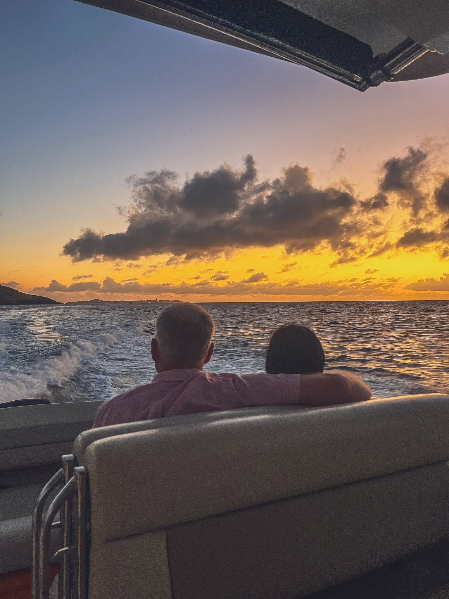 A man and a woman are sitting on a boat watching the sunset over the ocean.