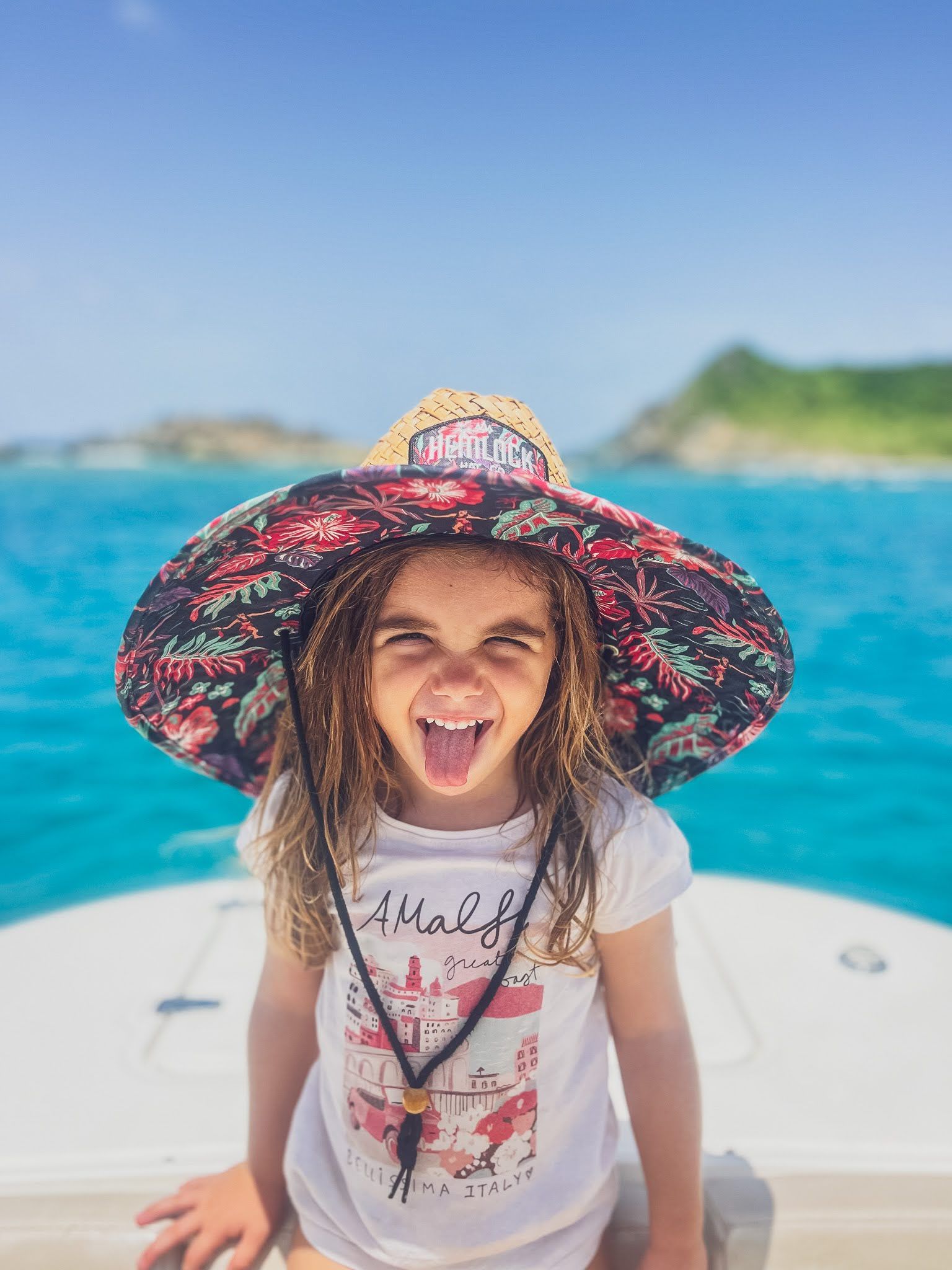 A little girl wearing a straw hat is sitting on a boat.