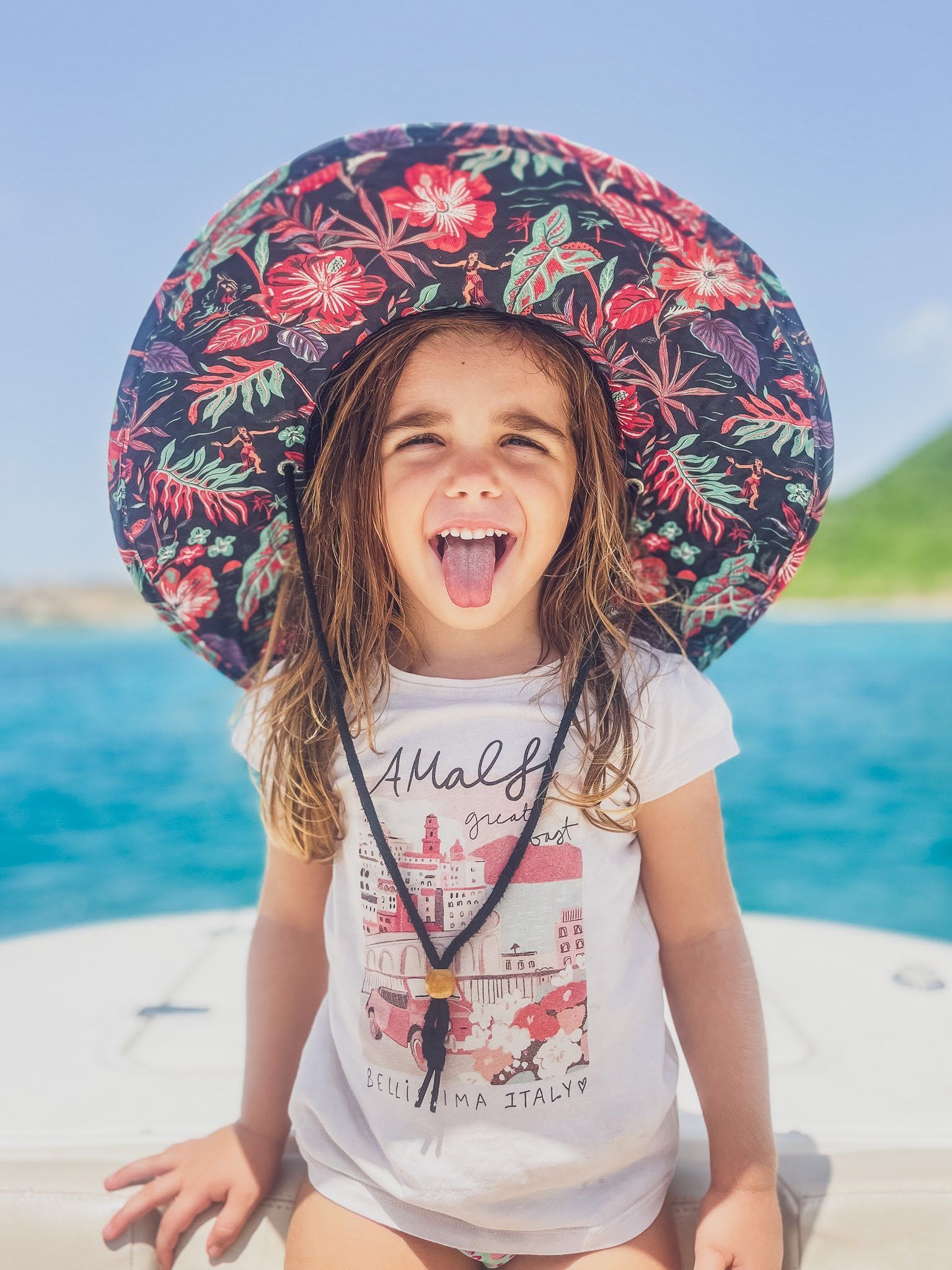 A little girl wearing a hat is sticking her tongue out.