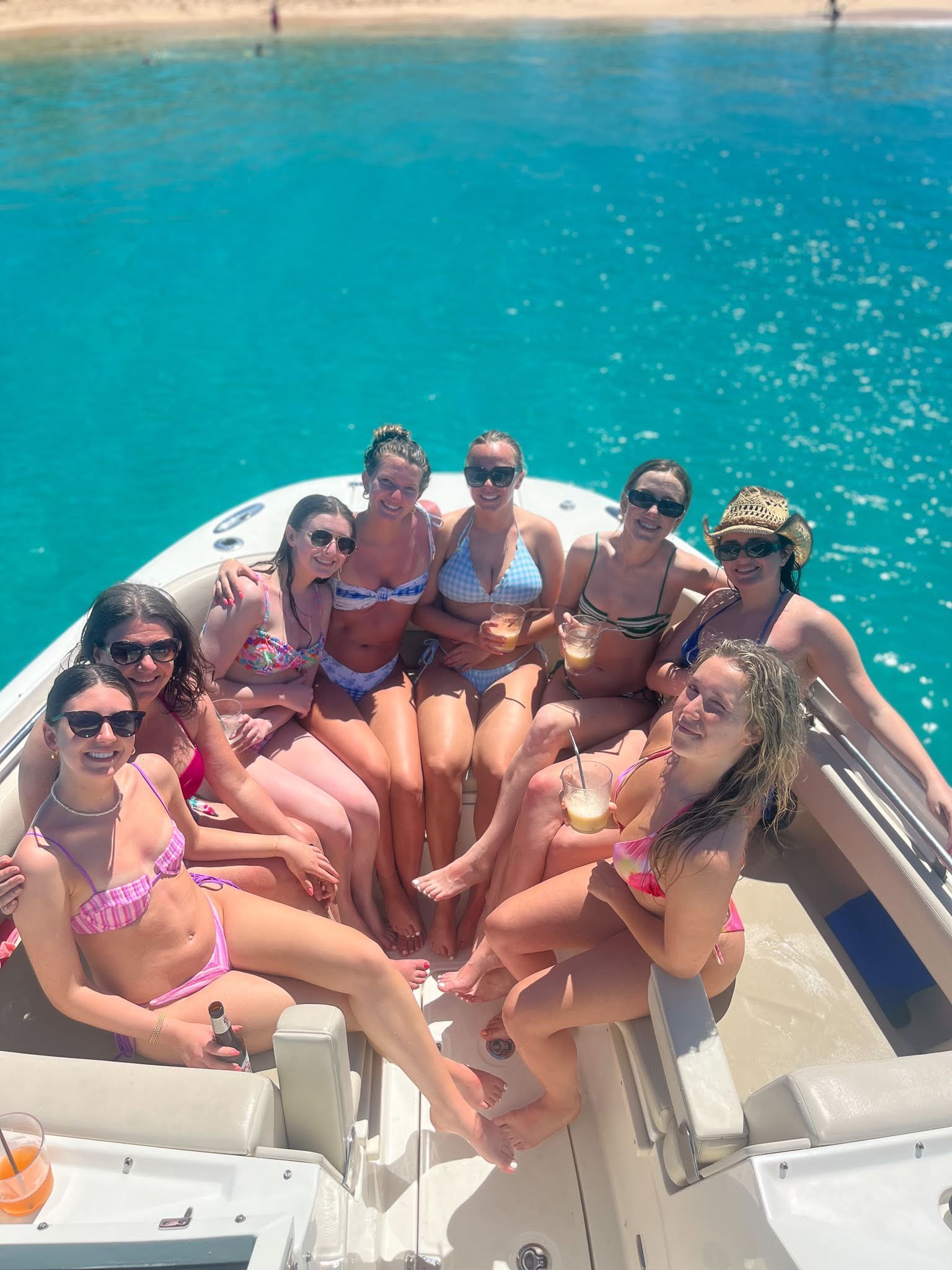 A group of women in bikinis are sitting on a boat in the water.