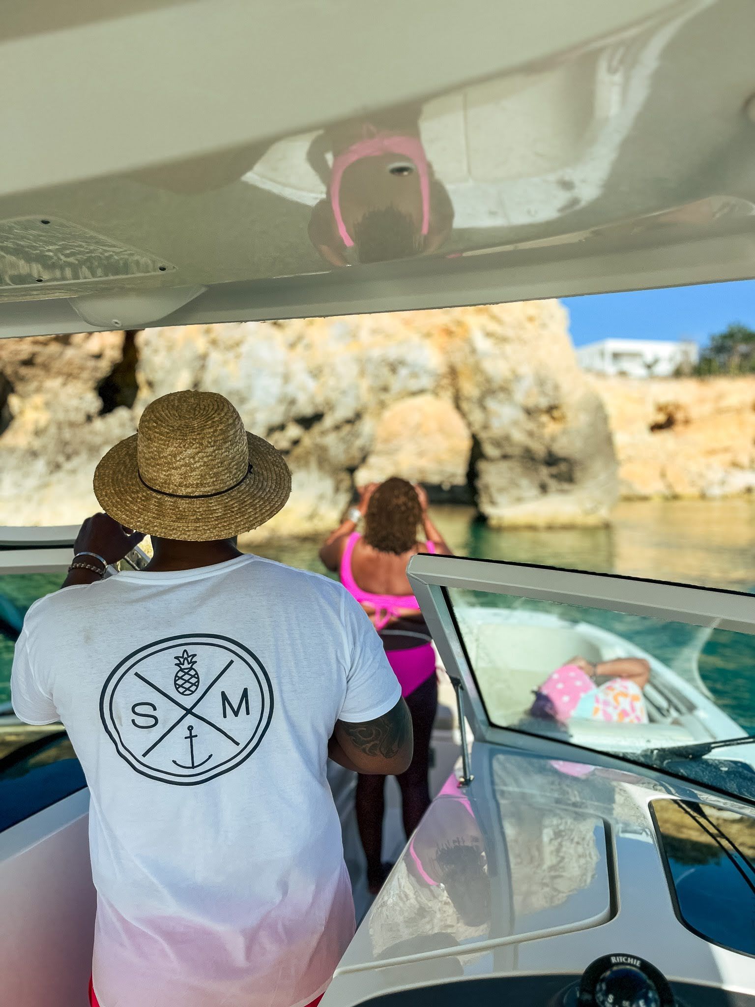 A man in a straw hat is standing on a boat looking at a woman in a pink bikini.