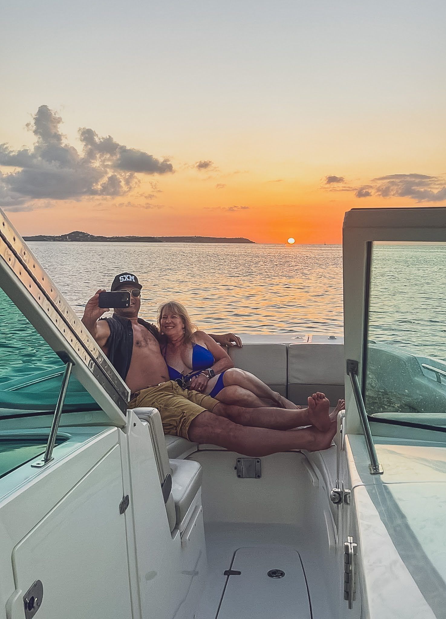 A man and a woman are laying on a boat in the ocean at sunset.